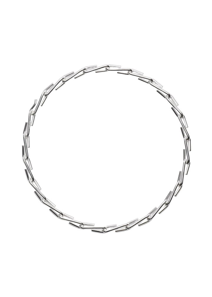 A silver-toned geometric chain necklace with elongated, angular links arranged in a circular shape, photographed against a clean, light gray background.