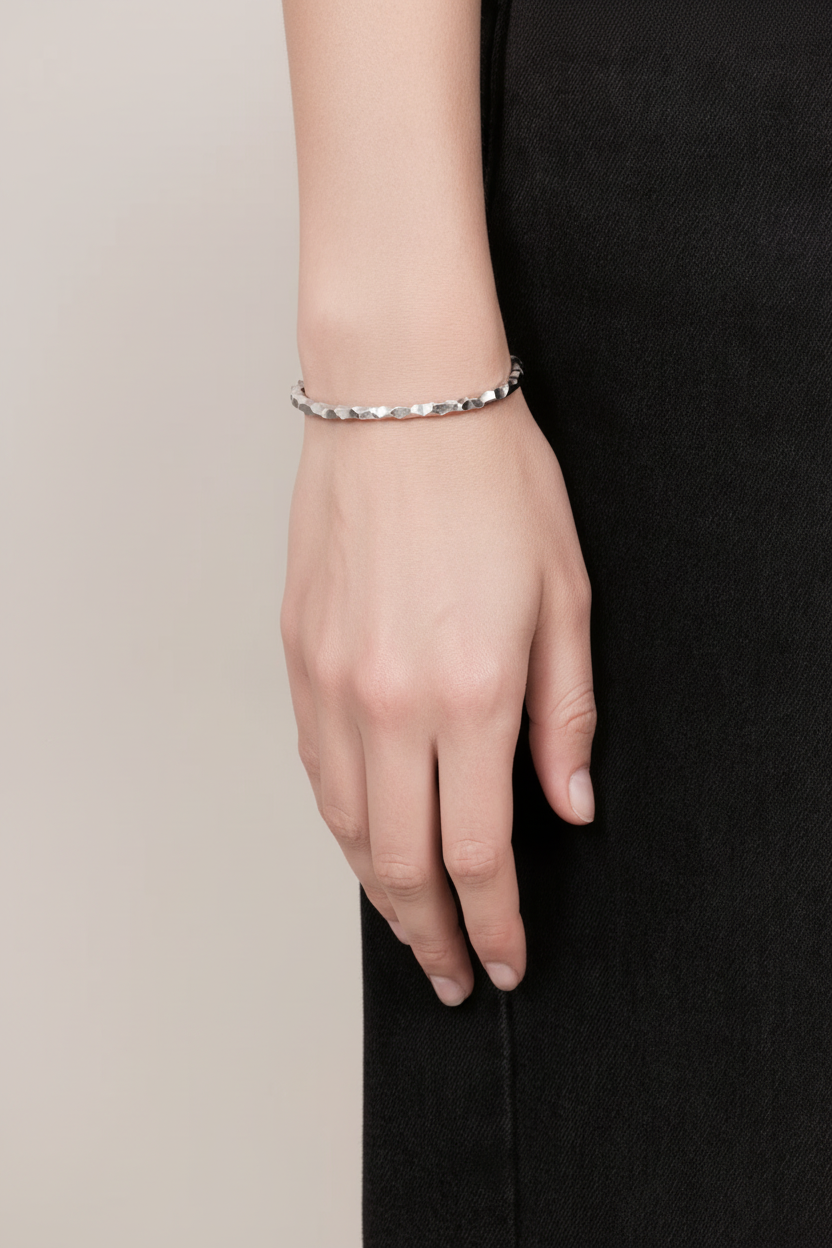 A close-up of a person's hand wearing a delicate silver beaded bracelet, set against a dark charcoal dress and a light beige background.
